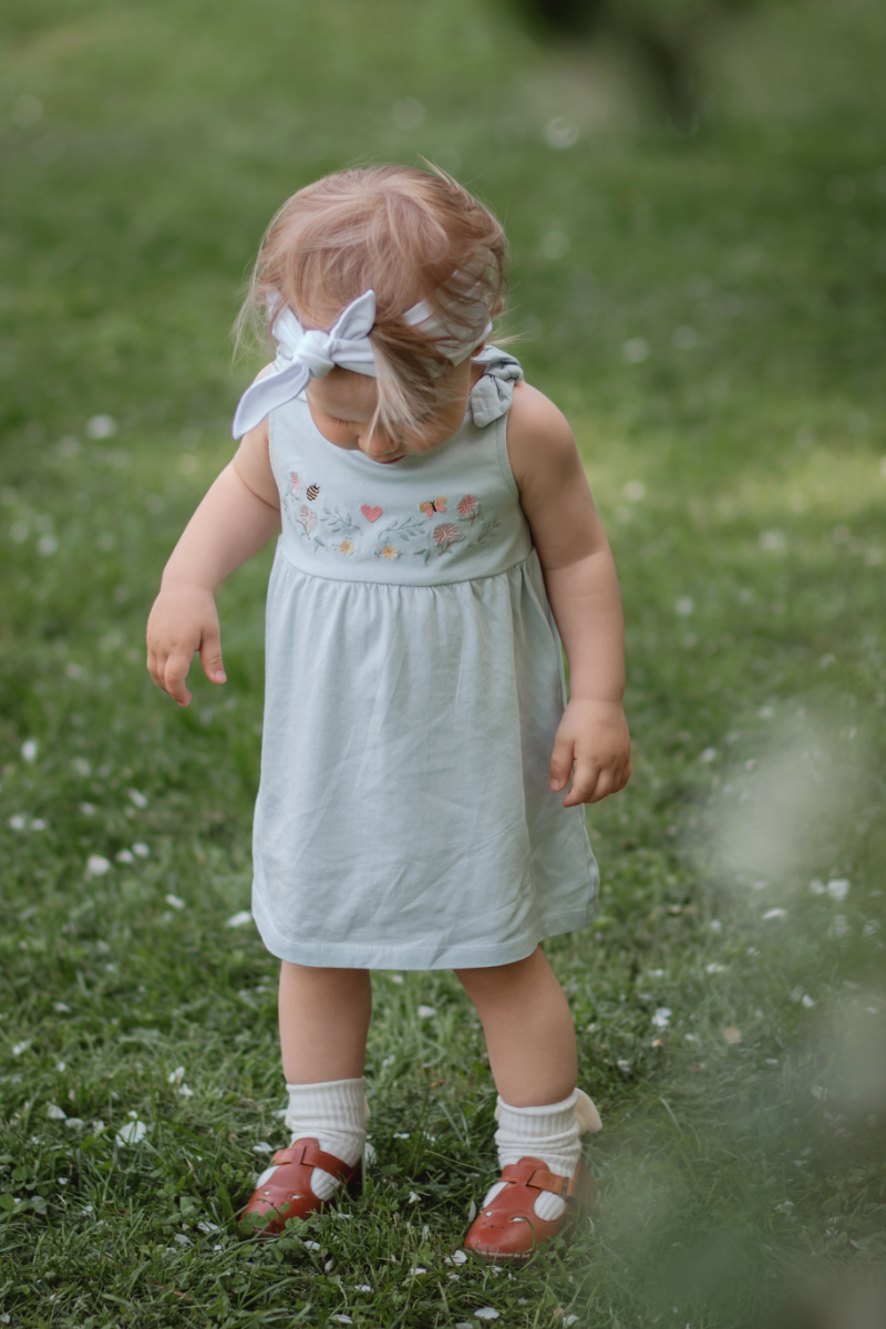 Mała dziewczynka w sandałkach stojąca na trawniku